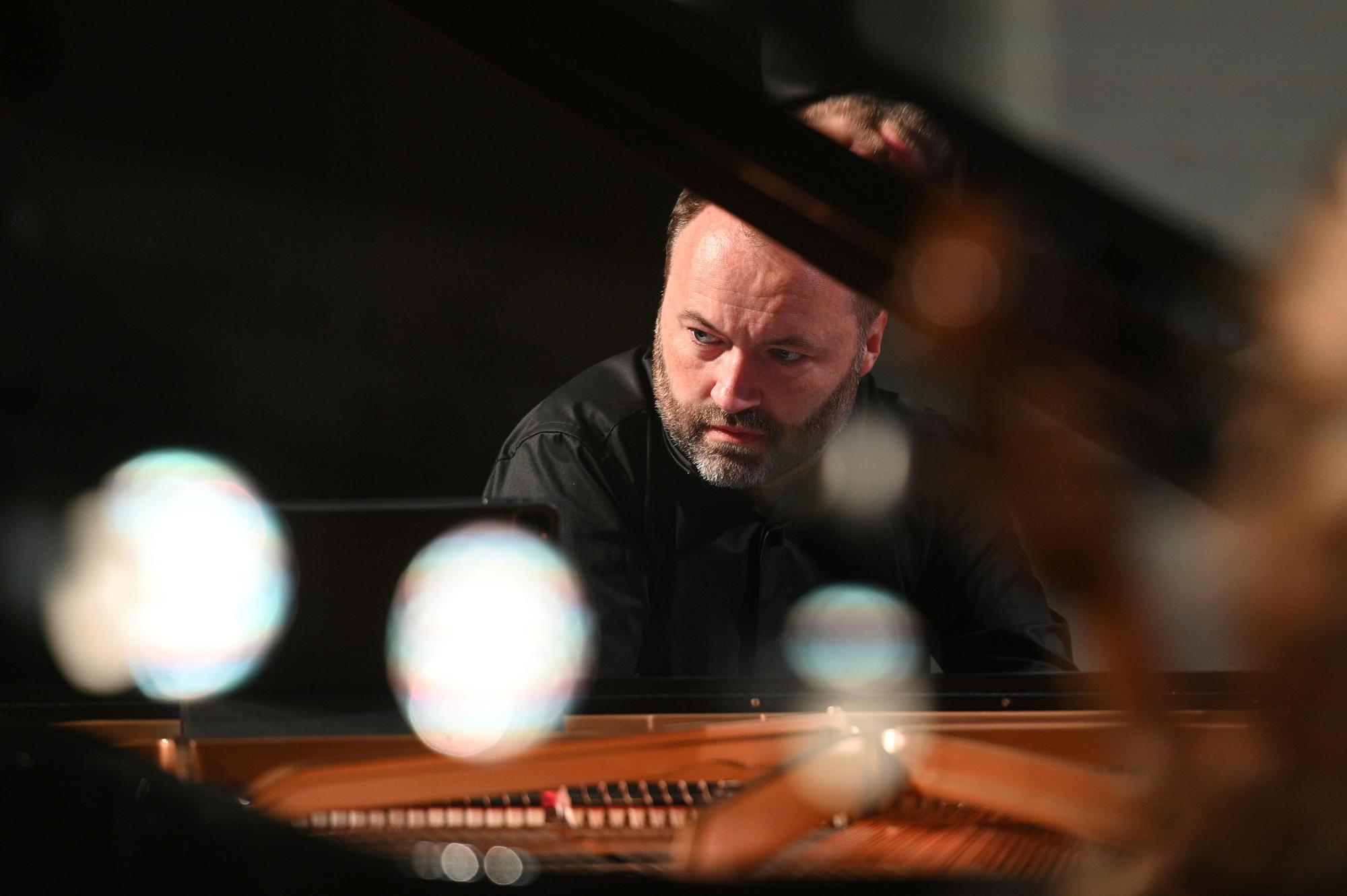 Piotr Sałajczyk, pianista ubrany w czarną koszulę i czarne spodnie, siedzi skupiony przy klawiaturze fortepianu