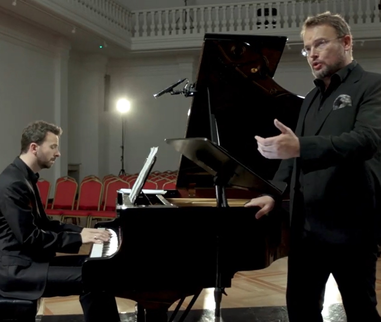 Bas baryton Tomasz Konieczny wykonuje pieśni Moniuszki z pianistą Lechem Napierałą, są ubrani w czarne stroje i muzykują przy czarnym dużym fortepianie