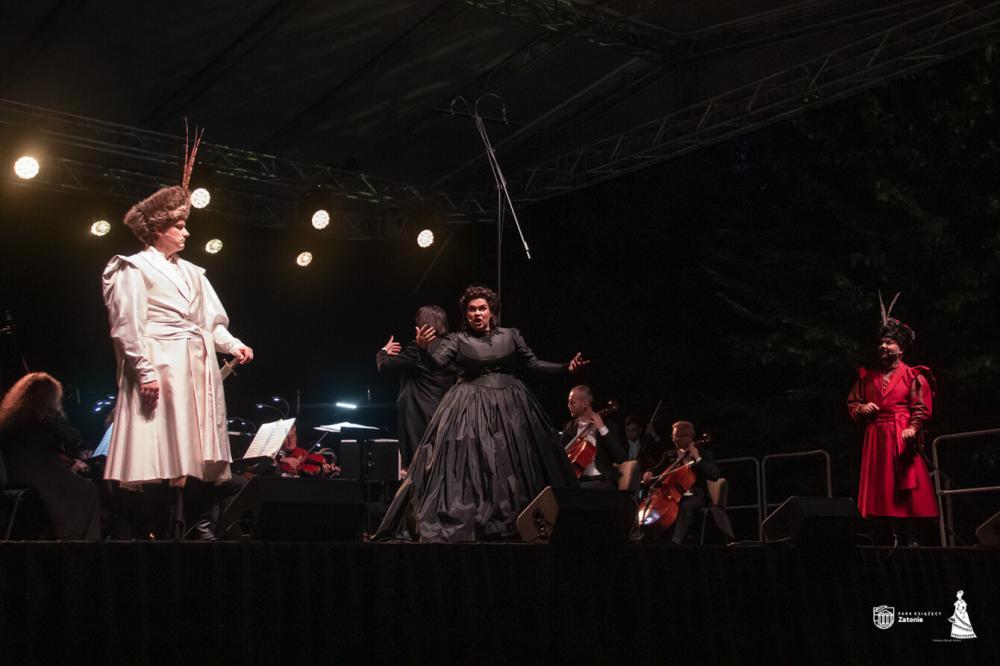 Soliści Polskiej Opery Królewskiej stoją na estradzie w strojach historycznych - białym surducie i czarnej sukni - i wykonują operę Straszny dwór Stanisława Moniuszki