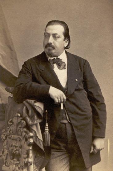 Kompozytor i skrzypek Henryk Wieniawski stoi oparty o poręcz schodów, jest ubrany w elehancki surdut i apaszkę