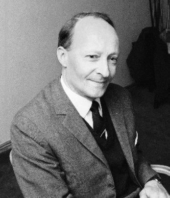 Kompozytor, pianista i dyrygent Witold Lutosławski pozuje siedząc na krześle, jest ubrany w jasny garnitur i ciemny krawat